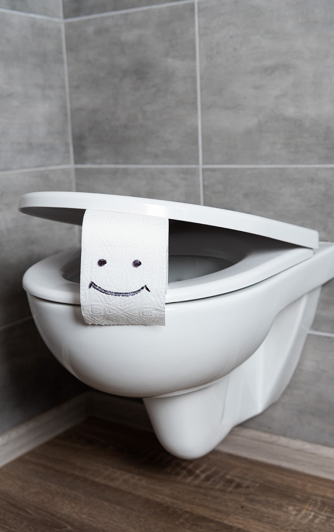 a toilet with toilet paper in the lid. the toilet paper has a happy face drawn on it.